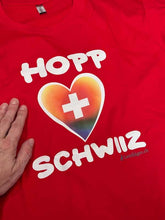 Lade das Bild in den Galerie-Viewer, T-Shirt in Rot, mit Hopp Schwiiz und einem farbigen (Regenbogen) Herz mit Schweizerkreuz